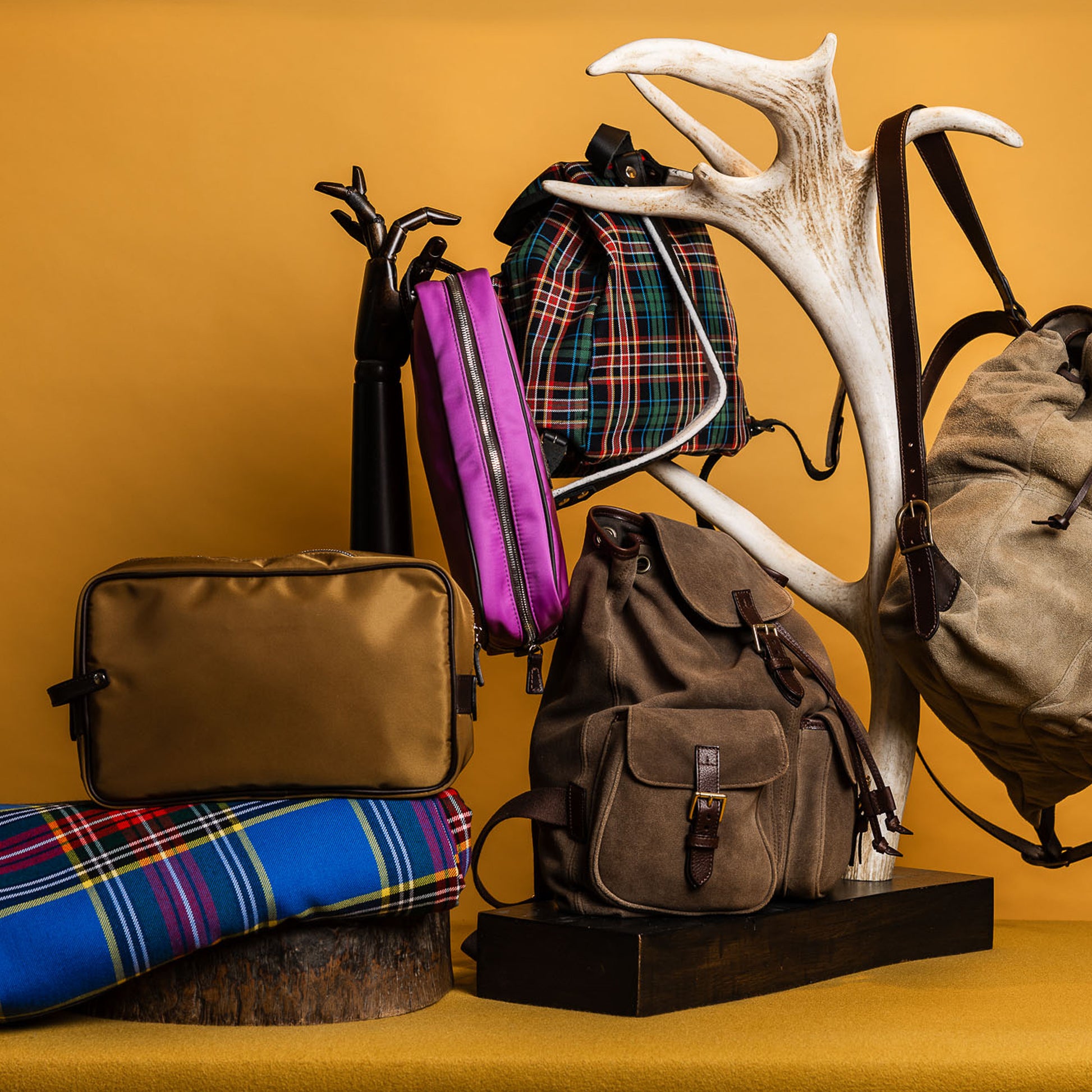 Brauner Rucksack und weitere Taschen auf gelbem Hintergrund neben Hirschgeweih
