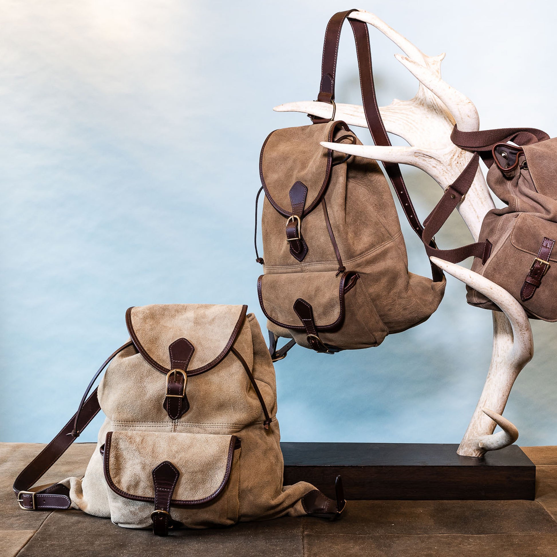 Drei Braune Rucksäcke vor blauem Hintergrund an Hirschgeweih hängend